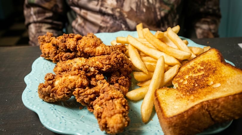 Crispy fried chicken tenders, golden french fries, and Texas toast on a scalloped blue plate.